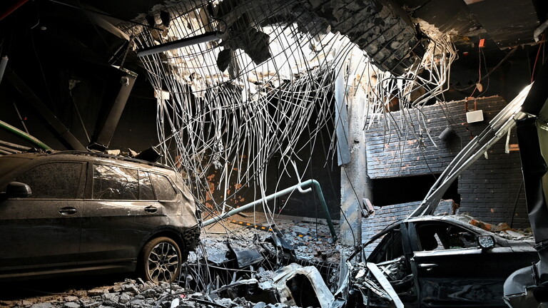 Kiew, Ukraine: Ein Loch in einer Geschossdecke durch eine Raketenexplosion und beschädigte Autos auf dem Parkplatz eines Wohngebäudes, das durch einen massiven russischen Raketenangriff beschädigt wurde.