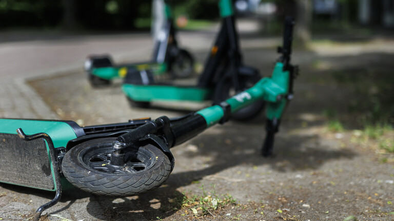 Im Vordergrund liegt ein E-Roller auf dem Boden, im Hintergrund stehen zwei weitere geparkt am Straßenrand.