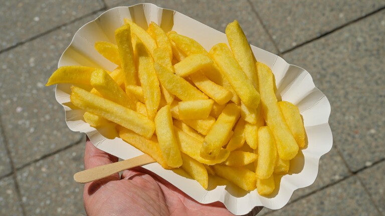 Ein Hand hält eine Schale Pommes frites