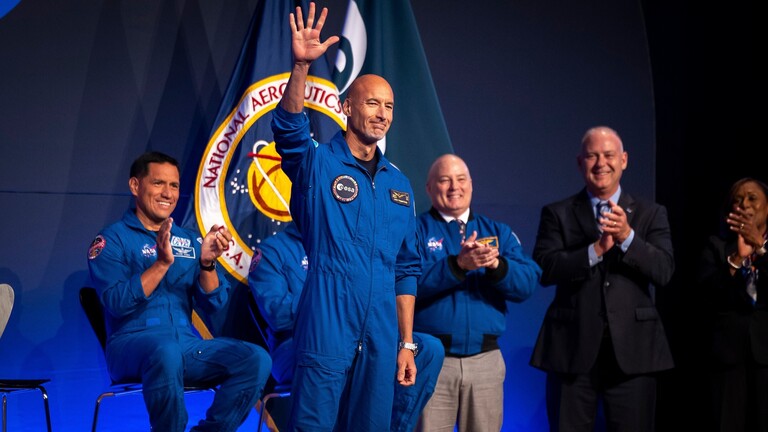 Luca Parmitano, Mitglied der Artemis-III-Besatzung, hebt während einer Pressekonferenz im Johnson Space Center einen Arm mit weit geöffneter Hand Richtung Publikum. Im Hintergrund applaudieren NASA-Vertreter.