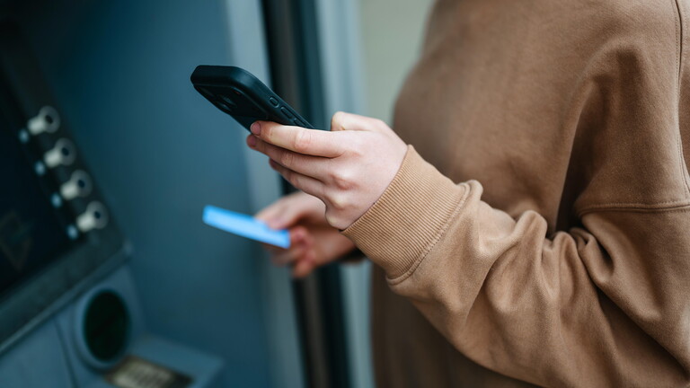 Eine junge Frau will Geld am Bankautomaten abheben