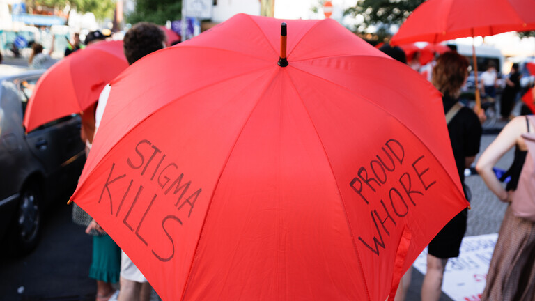 Demonstrationsteilnehmende tragen rote Schirme, unter anderem mit der Aufschrift "Stigma Kills" und „Proud Whore" bei einer Kundgebung von Aktivisten gegen ein Verbot von Straßenprostitution und für den Erhalt des Frauentreffs Olga in Berlin.
