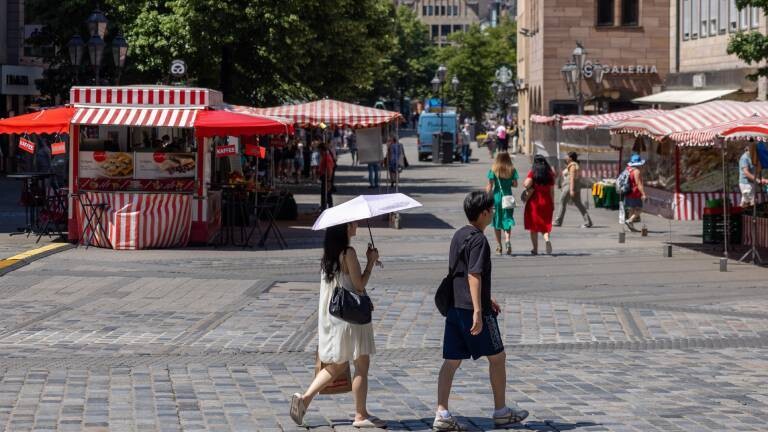 Die Fußgängerzone Nürnbergs an einem sonnigen Junitag. Menschen schützen sich mit Schirm und Hut.