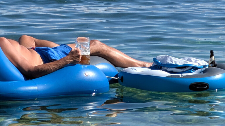 Mann liegt auf Luftmatratze im Starnberger See, Bayern, mit Bier in der Hand