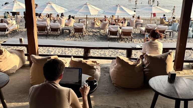 Touristen sitzen mit Smartphone und Laptop in einem Strandcafé