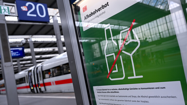 Am Bahnsteig an einem Bahnhof hängt ein Hinweis auf das Alkoholverbot der Deutschen Bahn. Auf grünem Grund sind eine Flasche und ein Glas abgebildet und durchgestrichen.