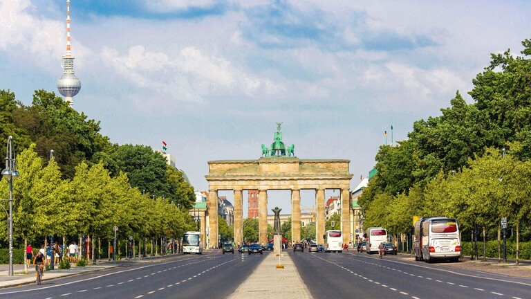 Auf der Straße des 17. Juni, die direkt auf das Brandenburger Tor zuläuft. Links sieht man den Fernsehturm Berlin. Rechts am Straßenrand stehen Reisebusse