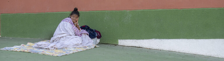 Junge Frau, in Decken gehüllt, sitzt an einer Wand in Ceuta (Spanien, 24.08.2026)