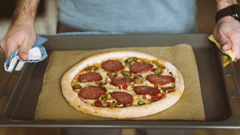 Ein Mann hält ein Ofenblech mit einer Tiefkühlpizza in den Händen.