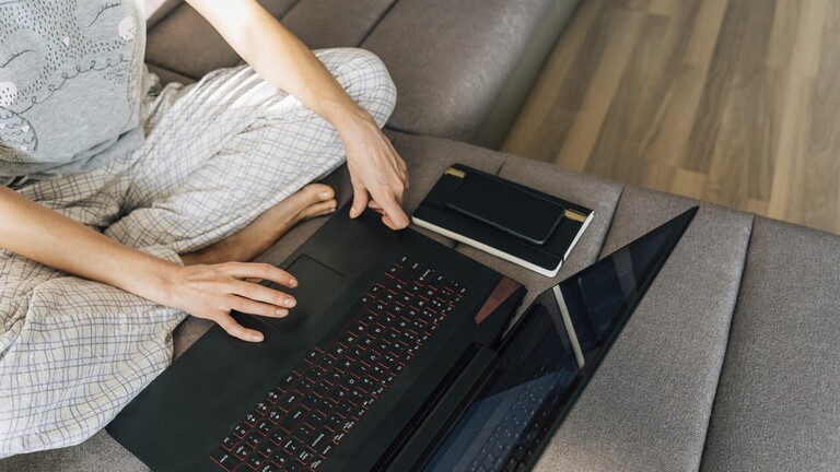 Eine Frau in Hauskleidung mit einem Laptop, neben ihr ein Notizbuch und ein Stift.