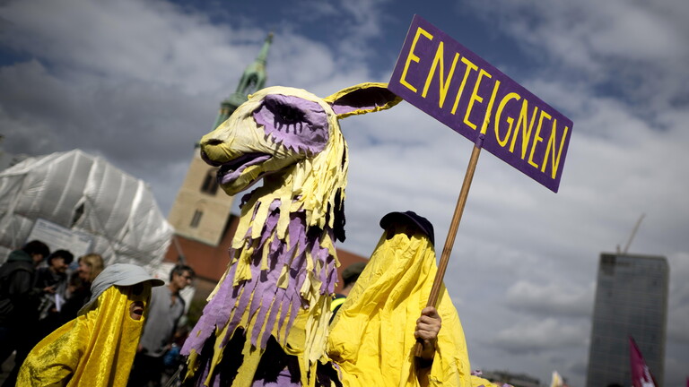 Demonstrant der Initiative Volksentscheid Deutsche Wohnen und Co ist als lila-gelbes Einhorn oder Trojanisches Pferd verkleidet und hält ein Schild mit dem Wort "Enteignung" in die Höhe (05.09.2026, Berlin)