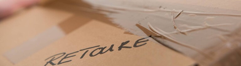 Eine Frau klebt ein Paket mit der Aufschrift Retoure mit Paketband zu.