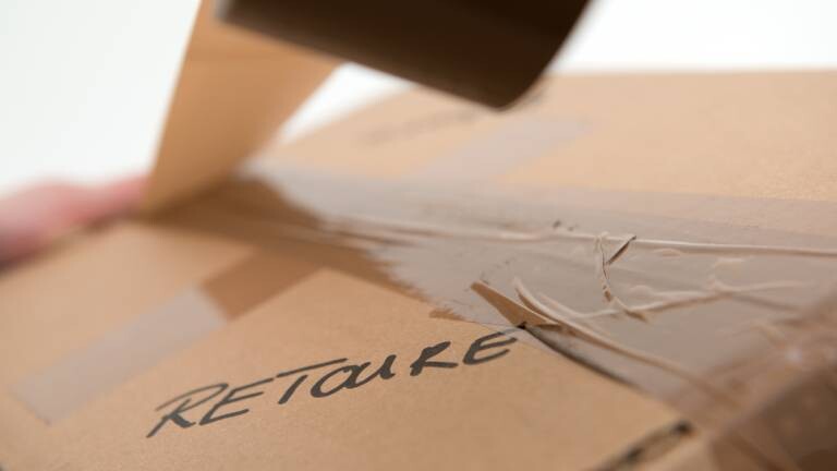 Eine Frau klebt ein Paket mit der Aufschrift Retoure mit Paketband zu.