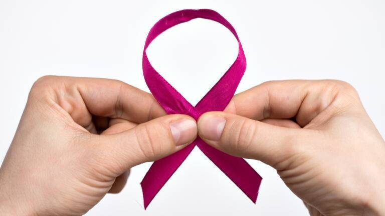 Der Weltkrebstag ist jährlich am 4.2. Anlässlich des Tages hält eine Person eine Krebsschleife als Symbol in der Hand.