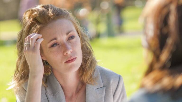 Frau mit besorgtem Gesichtsausdruck sitzt schweigend einer anderen Person gegenüber