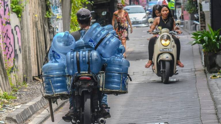 Mann transportiert mit einem Moped große Wasserbehälter in Kuta, Indonesien