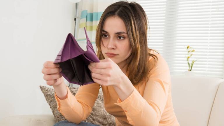 Eine Frau sitzt in ihrer Wohnung und hält ein leeres Portemonnaie in der Hand.
