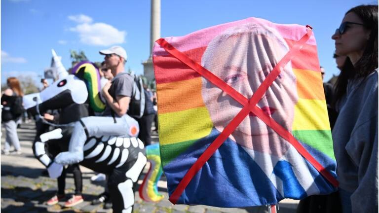 Demonstrantin hält durchgestrichenes Bild mit geschminkten ungarischen Premierministers Viktor Orban auf einer Regenbogenfahne (12.4.2025)