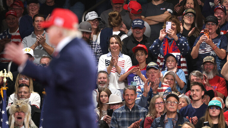 Anhänger sitzen bei einer Wahlkampfveranstaltung anläslich der Midterms in der Majestic Valley Arena in Kalispell; im Vordergrund steht US-Präsident Donald Trump zu sehen (14. Oktober 2026, Montana, USA)