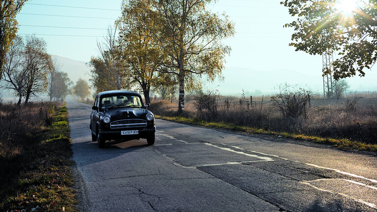 Foto eines alten indischen Autos der Marke Ambassador auf einer baumgesäumten Landstraße
