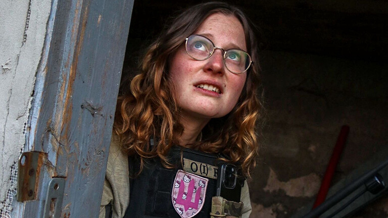 Foto von Anna Elsbernd, die mit ihrer Organisation "Universal Aid Ukraine" in der Ukraine Menschen aus Kriegsgebieten evakuiert: Sie sitzt mit einer Schutzweste bekleidet in einem Gebäude und schaut durch eine Türöffnung besorgt in den Himmel.
