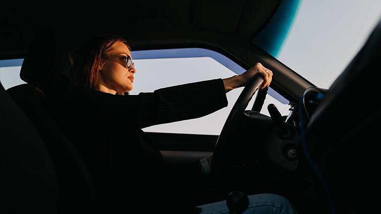Foto einer jungen Frau, die mit Sonnenbrille am Steuer eines Autos sitzt
