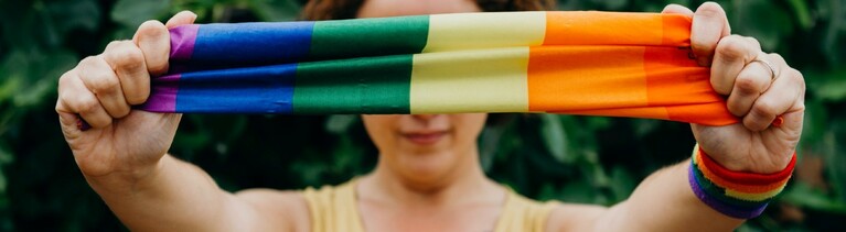Junge Frau hält ein regenbogenfarbenes Tuch in die Kamera.