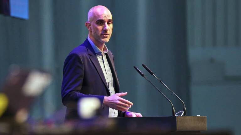 Belit Onay steht vor einem Rednerpult und zwei Mikrofonen. Er spricht. Es ist eine Menge Staub in der Luft.