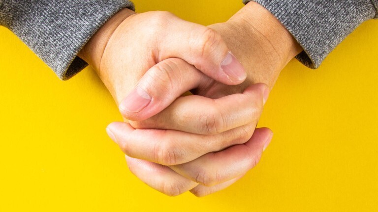 Die Hände des Mannes zum Gebet gefaltet auf gelben Hintergrund.