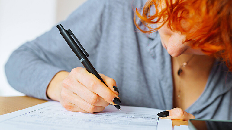 Foto einer jungen, rothaarigen Frau, die mit einem Stift ein Bewerbungsformular ausfüllt