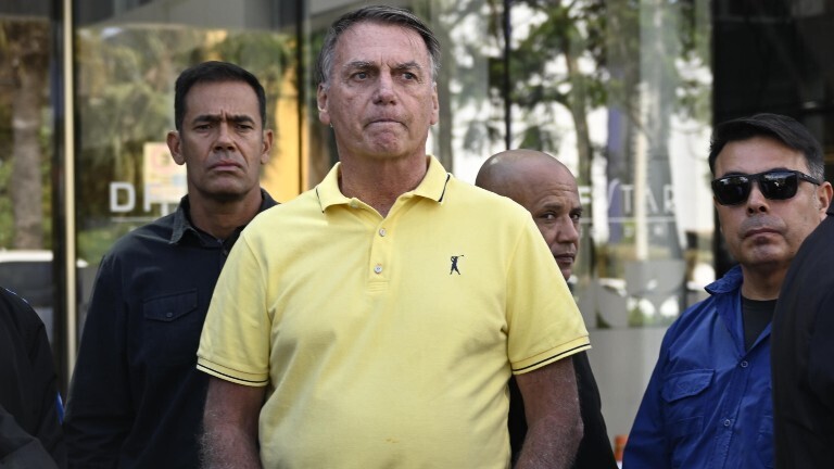 Brasiliens Ex-Präsident Jair Bolsonaro steht in einem gelben Poloshirt vor einem Krankenhaus und wartet.