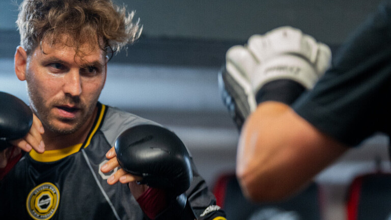 Markus Marsch beim Training im Kampfsportstudio: Er trägt Sportkleidung und einen Handschutz, während er gegen eine andere Person Schläge ausführt.