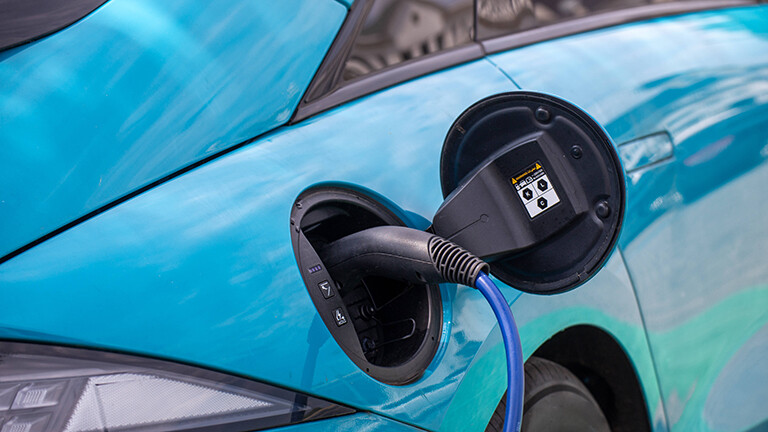 Nahaufnahme eines Ladesteckers, der in der geöffneten Ladeklappe eines blauen E-Autos steckt