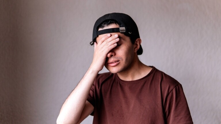 Ein gestresster Mann mit Baseballcap hält sich die rechte Hand vor die Augen.