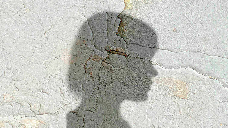 Schatten vom Kopf einer Frau auf einer rissigen Mauer.