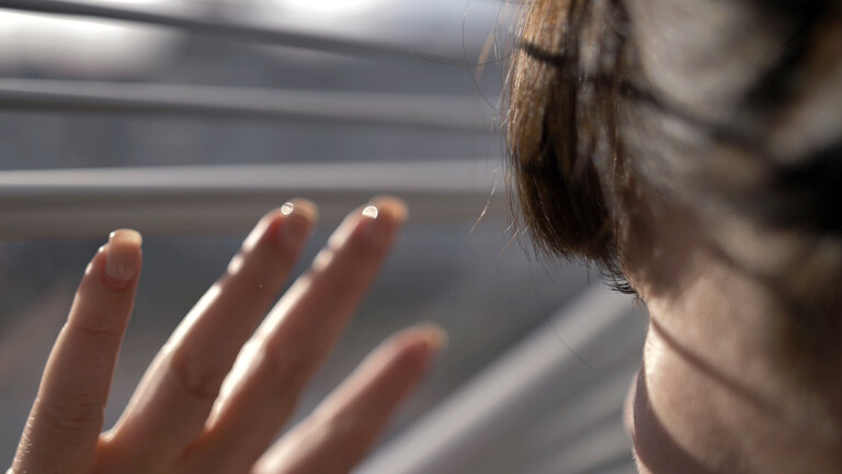 Eine Frau blickt durch eine Jalousie.