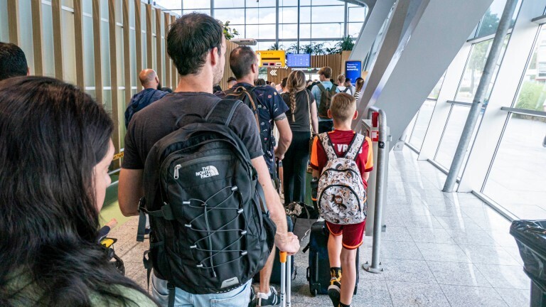 An einem Flughafen stehen Reisende in einer langen Schlange hintereinander.