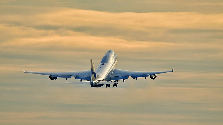 Foto einer startende Boeing 747 der Lufthansa am Frankfurter Flughafen, die vor einem orangefarbenen, bewölkten Abendhimmel aufsteigt.
