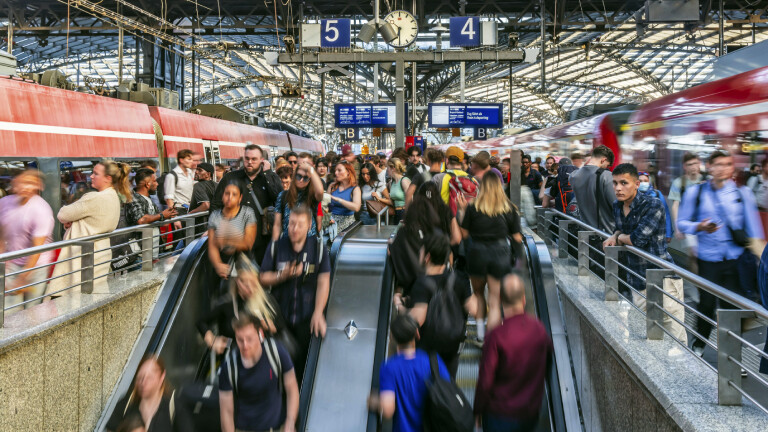 Viele Menschen auf einem Bahnsteig. Manche stehen und warten andere benutzen Rolltreppen. Es sieht voll aus.