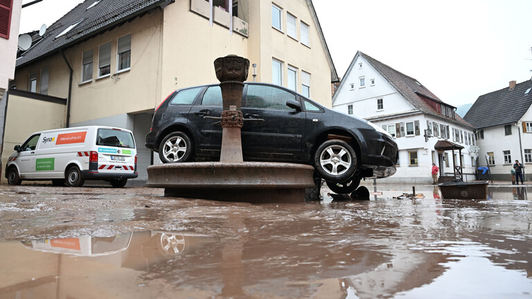 Auf einem Brunnen steht ein durch ein Hochwasser weggespültes Auto.