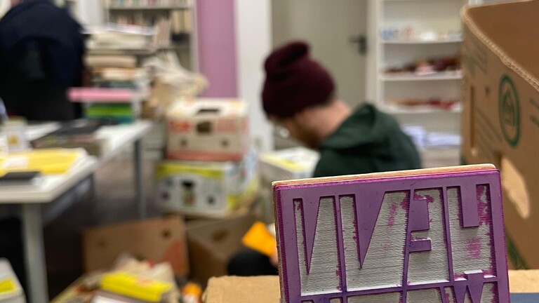 Ein junger Mann sitzt im Antiquariat der Buchgenossenschaft Hennwack und packt Bücher in Kartons.