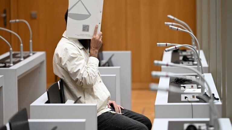 In einem Gerichtssaal sitzt der Angeklagte Sulaiman A.. Er verdeckt sein Gesicht mit einer Aktenmappe. Der Angeklagte hat am 31. Mai 2024 auf dem Mannheimer Marktplatz fünf Menschen mit einem Messer angegriffen und einen Polizisten tödlich verletzt.