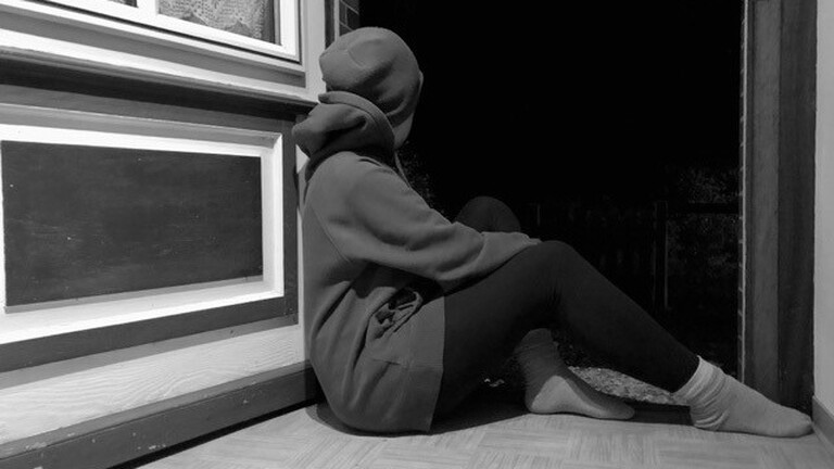 Person von hinten, die in einem Türrahmen sitzt
