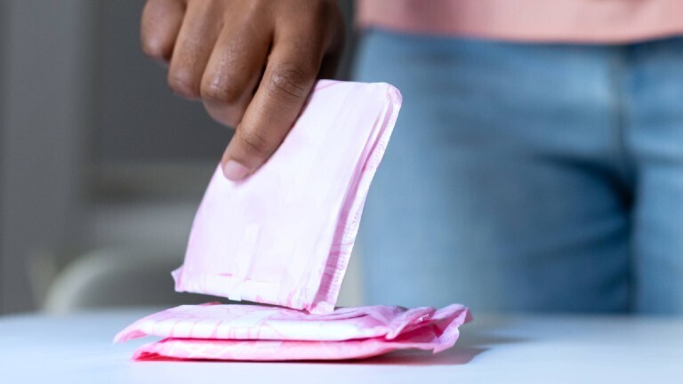 Auf einem Tisch liegen mehrere einzeln verpackte Binden. Eine Frau nimmt sich eine Binde aus dem Stapel.