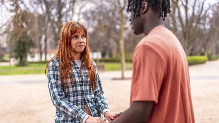 Eine junge Frau und ein junger Mann stehen sich gegenüber. Sie halten Händchen.