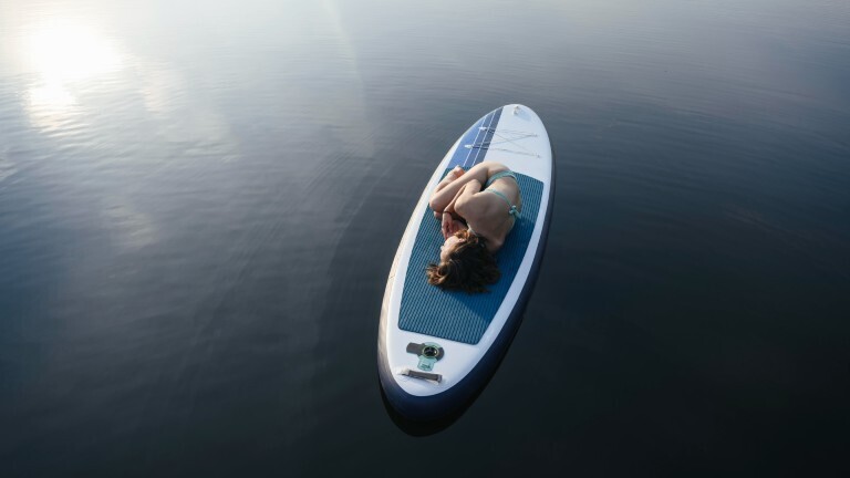 Eine Frau liegt in Embryo-Stellung auf einem Stand-up-Paddelboot.