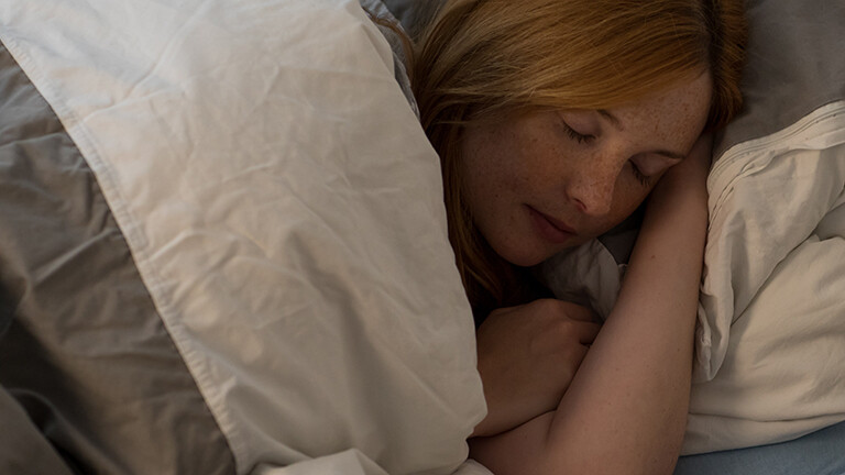 Foto einer jungen Frau, die im Bett auf der Seite schläft.