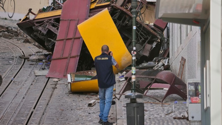 In Lissabon ist eine Standseilbahn entgleist. Auf dem Bild sieht man, wie Einzelteile der Seilbahn an einer Hauswand liegen. Ein Polizist fotografiert die Unfallstelle.