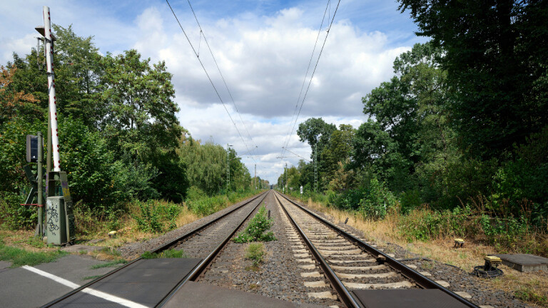 Zweigleisige Eisenbahnstrecke an geöffnetem Bahnübergang mit Schranke
