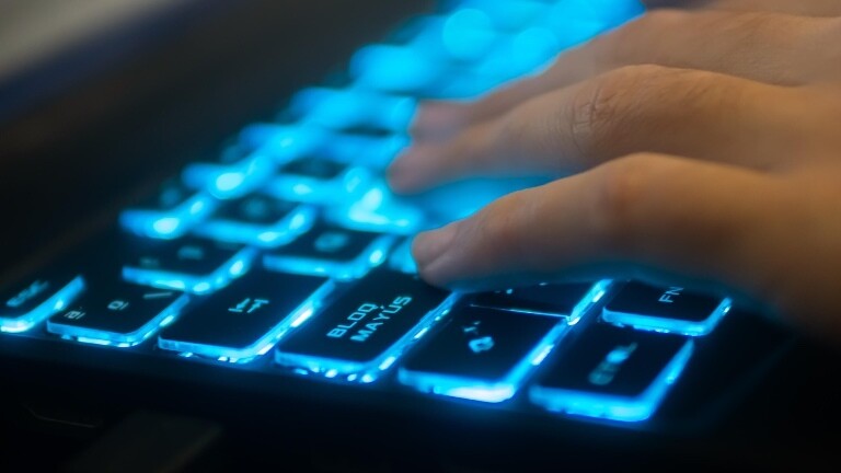 Jemand tippt auf einer Computertastatur, die blau aufleuchtet.
